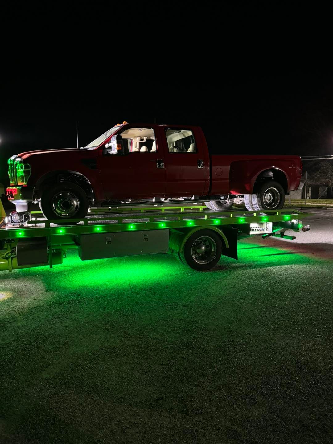 Red pickup truck on a tow truck with green underglow at night.