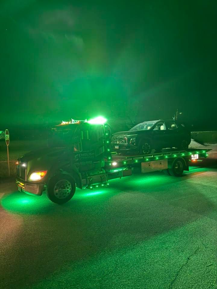 Tow truck with green lights, night scene, carrying a dark car.