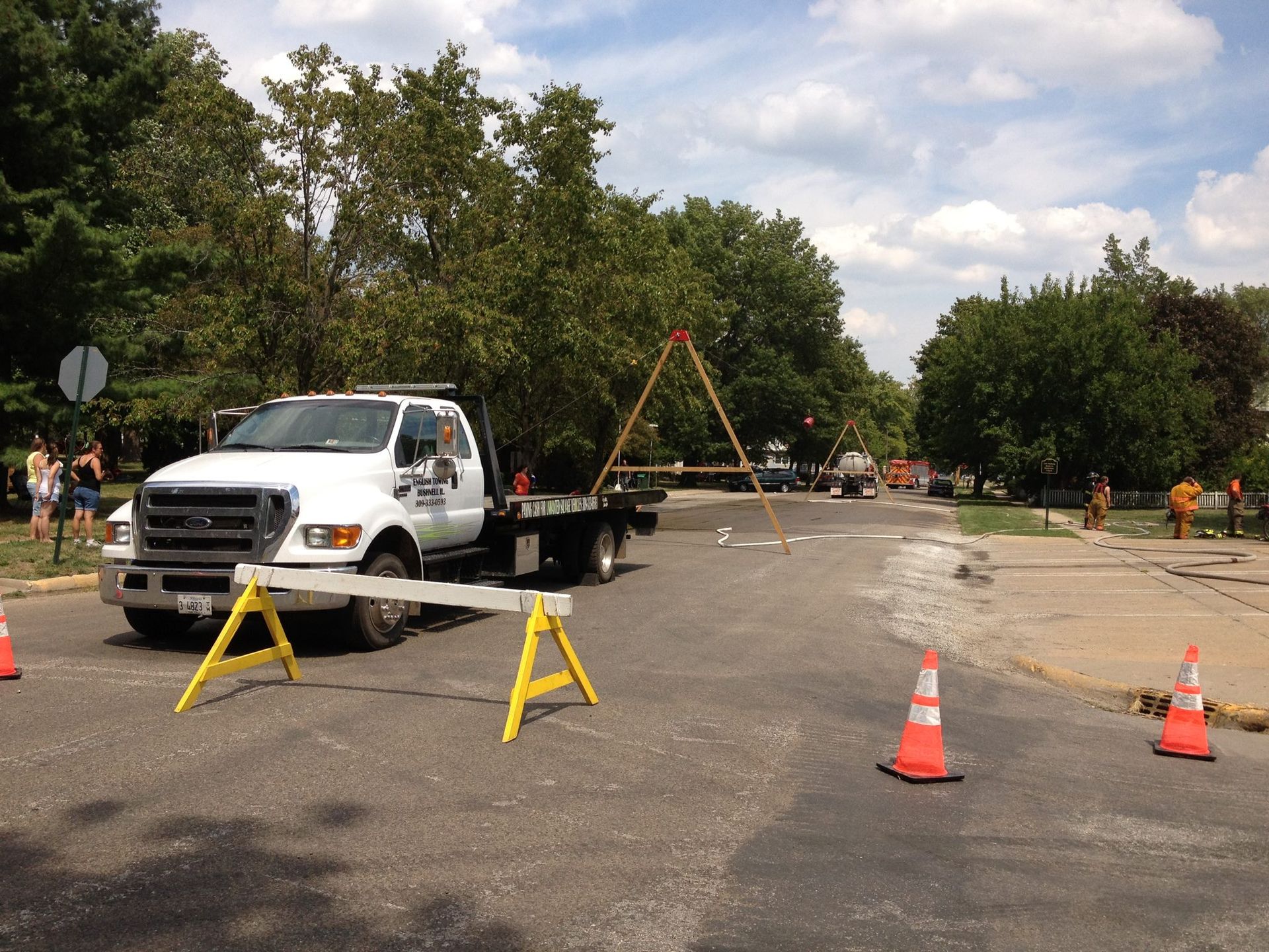 White truck with a crane in a road, blocked by traffic cones and sawhorses. Roadwork in progress.