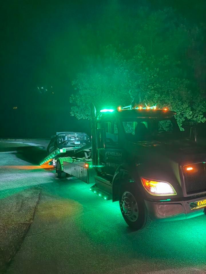 Tow truck with green lights loading a dark vehicle at night.