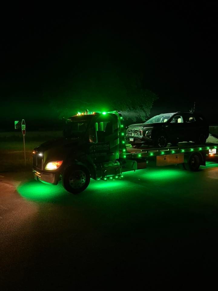 Tow truck with green underglow lights carrying a black SUV at night.