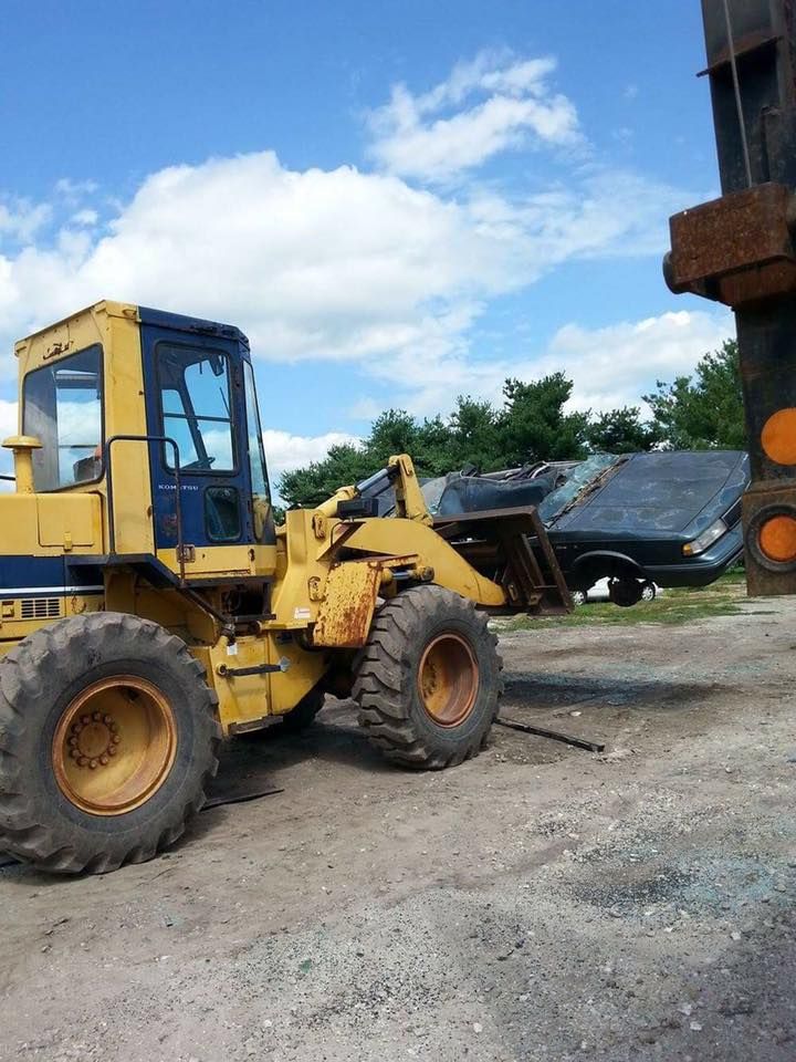 Yellow loader holding a crushed car, near a metal structure, under a blue sky.