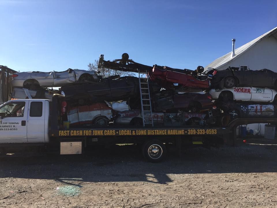 White truck loaded with crushed cars; metal ladder leaned against the pile.