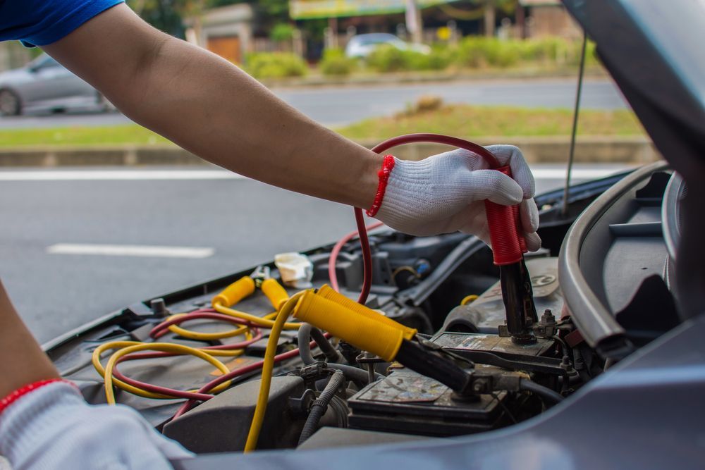 Person using jumper cables to jump-start a car battery on a roadside.