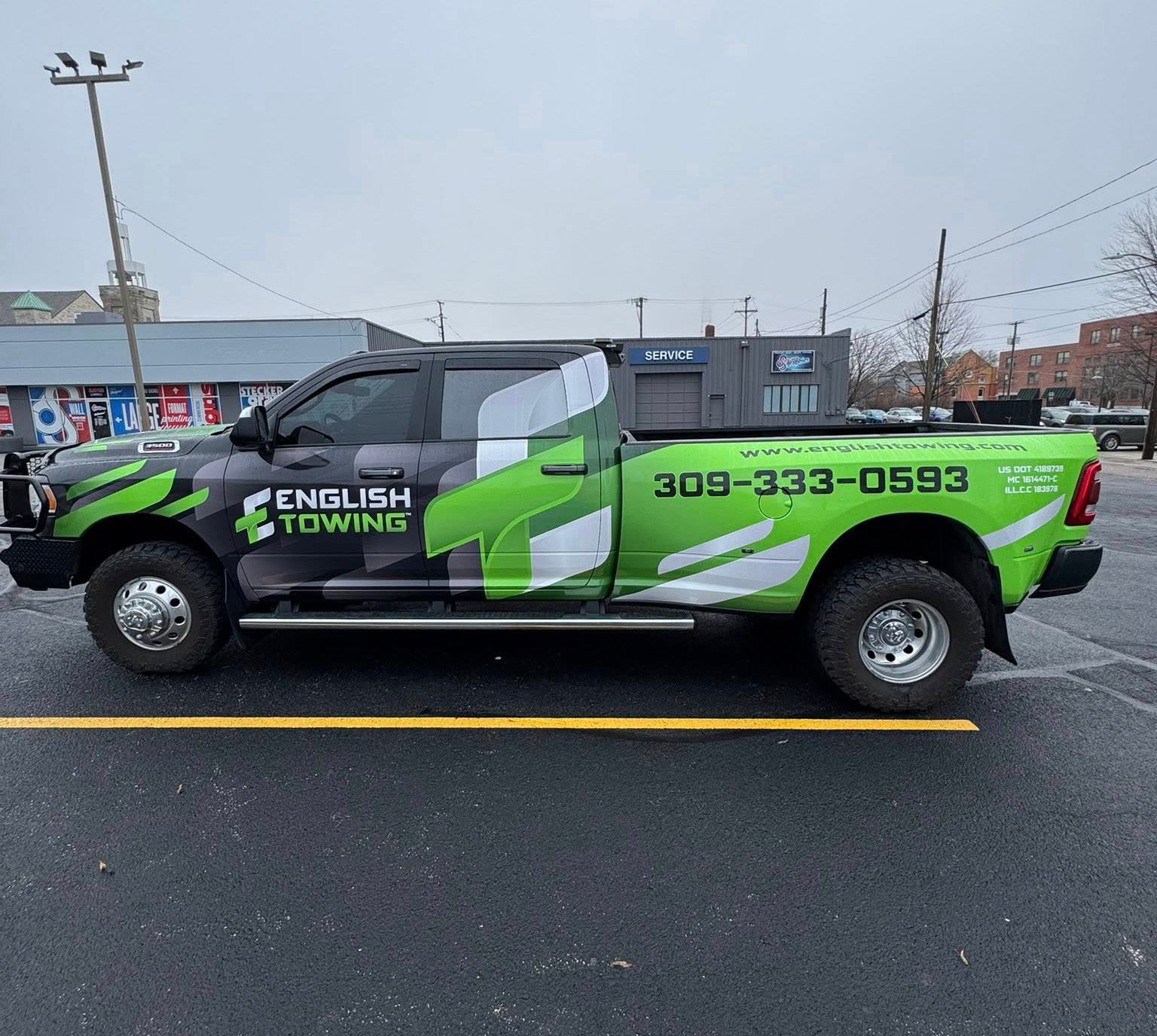 A tow truck with green and black camouflage wrap and English Towing logo parked on a street.