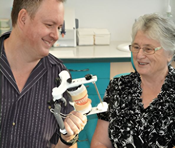 A Man and a Woman Are Looking at a Model of Teeth — Maroochy Denture Clinic In Yandina, QLD