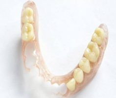Partial denture with light pink base and yellow artificial teeth, resting on a white surface — Maroochy Denture Clinic In Yandina, QLD