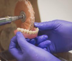 Hands in purple gloves polishing a set of dentures with a buffing wheel — Maroochy Denture Clinic In Yandina, QLD