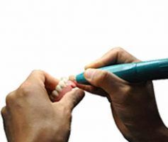Hands holding a dental tool, working on a set of dentures — Maroochy Denture Clinic In Yandina, QLD