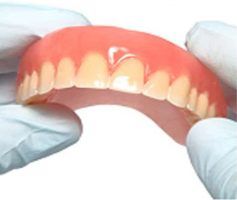 A person holding a set of dentures, with a pink gum area and artificial teeth — Maroochy Denture Clinic In Yandina, QLD