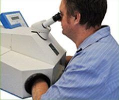 Man looking into a large, white machine with a microscope-like eyepiece; a blue screen sits on the machine — Maroochy Denture Clinic In Yandina, QLD