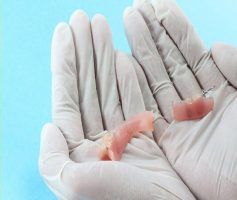Hands in gloves holding two partial dentures — Maroochy Denture Clinic In Yandina, QLD