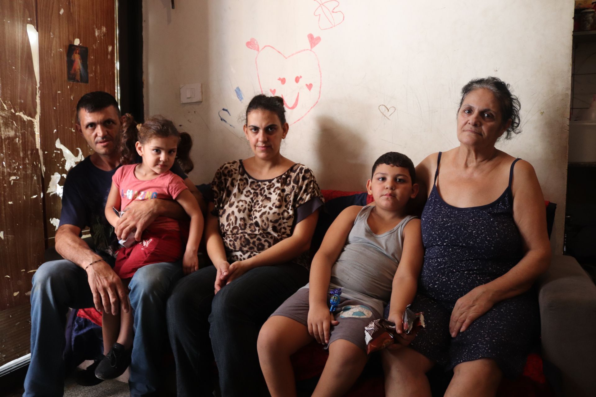 Family of five sitting on a sofa in a home. The wall behind them is decorated with a painted bear.