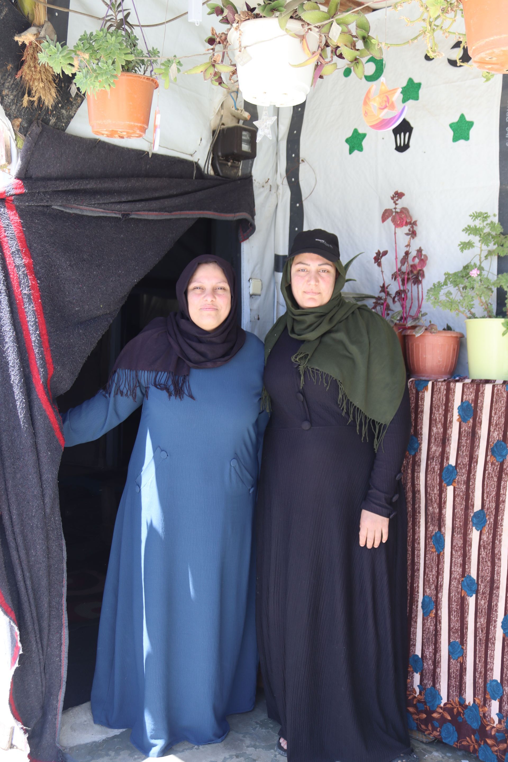 A husband and wife stand in front of a home at a refugee camp