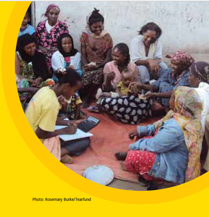 A group of women sit outdoors, some looking at a calculator, appearing to be in a meeting.
