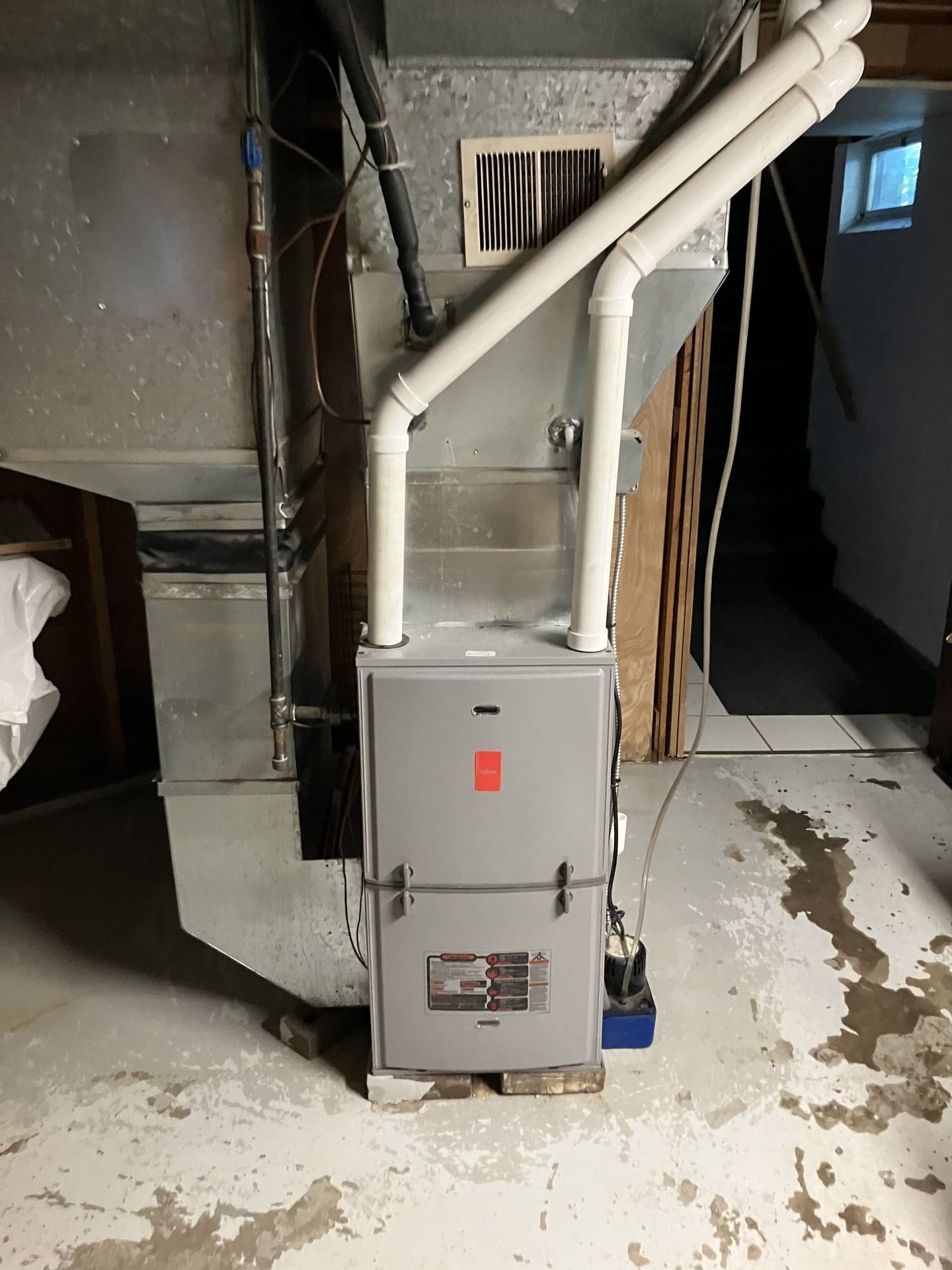 Gray furnace in a basement setting with white pipes.