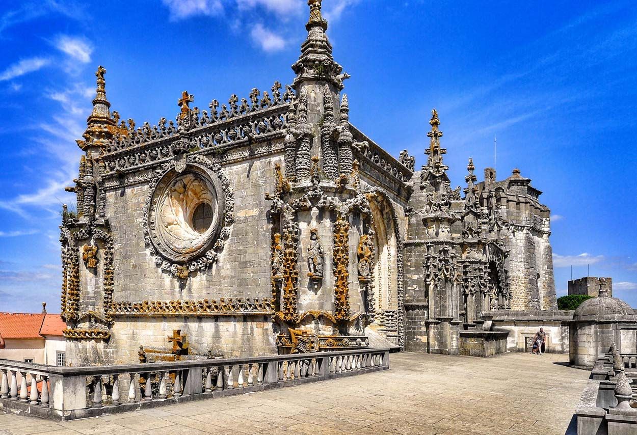 Igreja histórica de pedra com entalhes ornamentados e uma janela circular sob um céu azul brilhante.