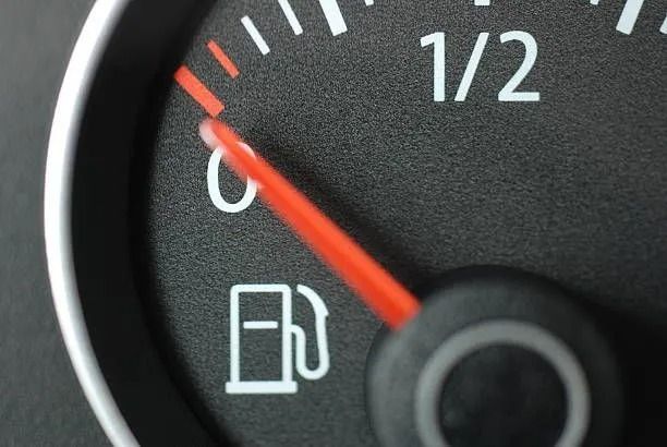 Close-up of a car fuel gauge with the needle near empty and a low-fuel icon lit