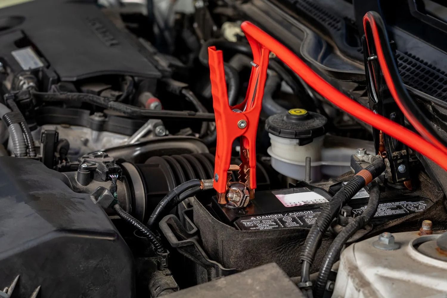 Red jumper cables clipped to a car battery in an engine bay