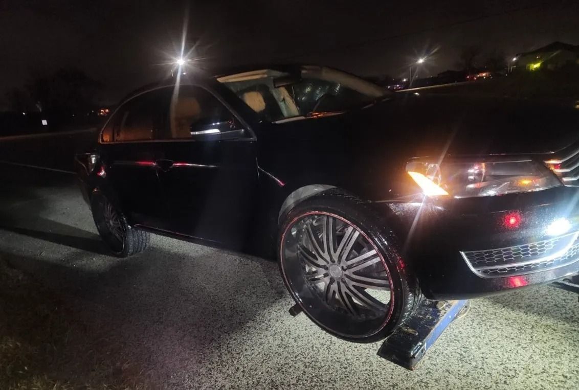 Black sedan parked at night with bright headlights on a wet road.