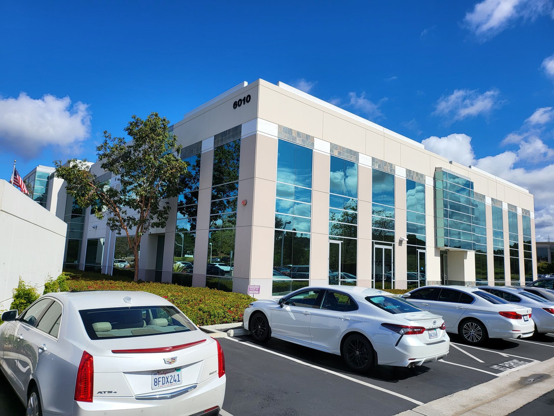 A row of white cars are parked in front of a large building.