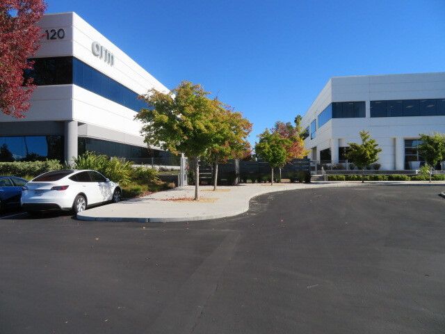 A white car is parked in front of a building with the number 120 on it