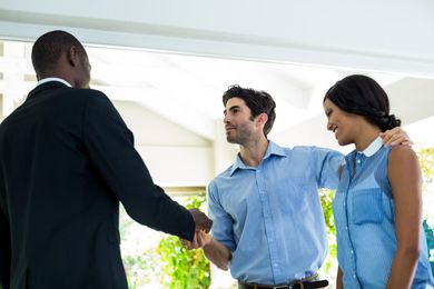 Three people shaking hands in a bright office corridor, suggesting a business meeting or introduction