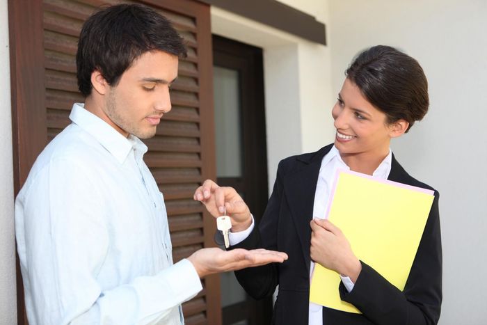 Two people exchanging keys at a doorway, one holding a yellow folder and smiling
