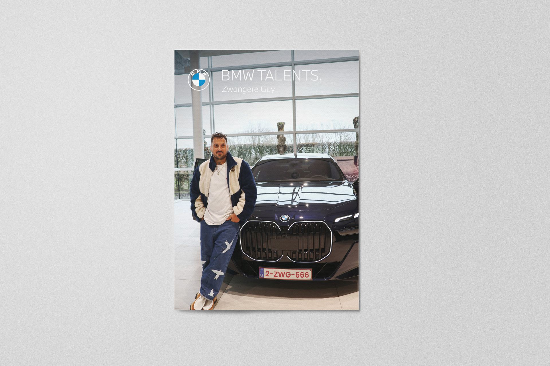 Een man in een jasje poseert naast een donkerblauwe BMW in een dealer. Het BMW-logo en 