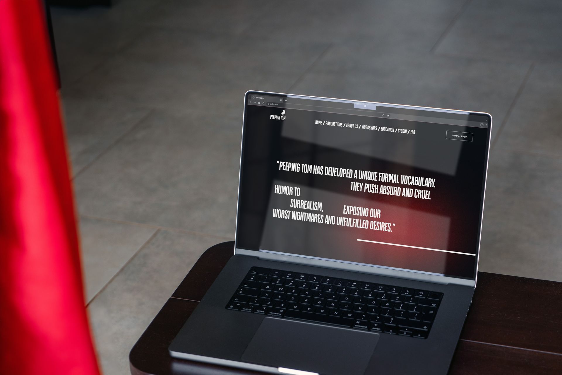 Laptop met tekst, mogelijk een website, op een tafel bij een rood voorwerp; binnenomgeving.