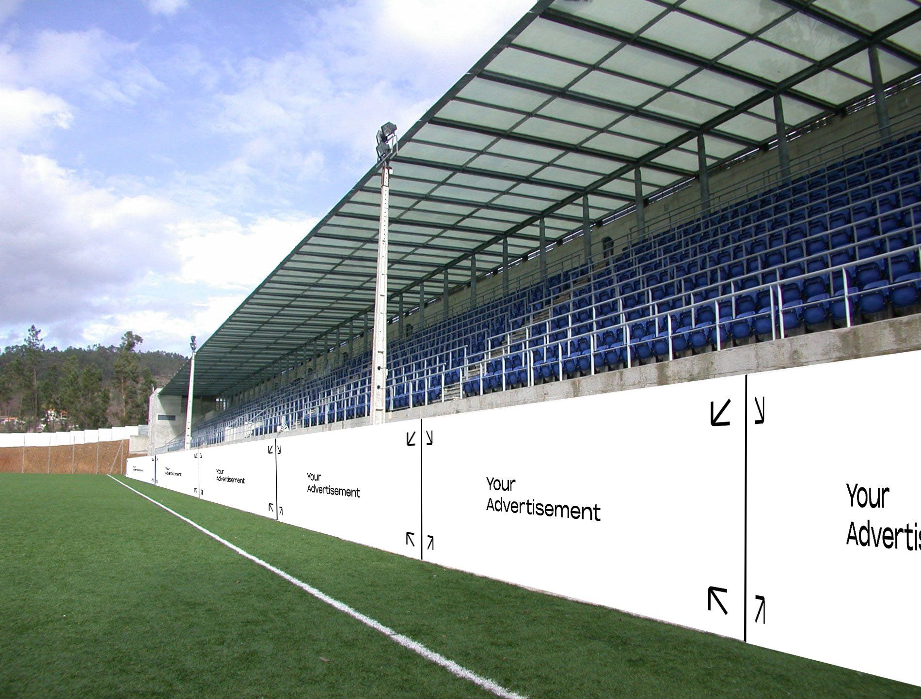 Uitzicht op een stadion met blauwe zitplaatsen en een groen veld. De witte muur langs het veld is voorzien van reclameruimte.