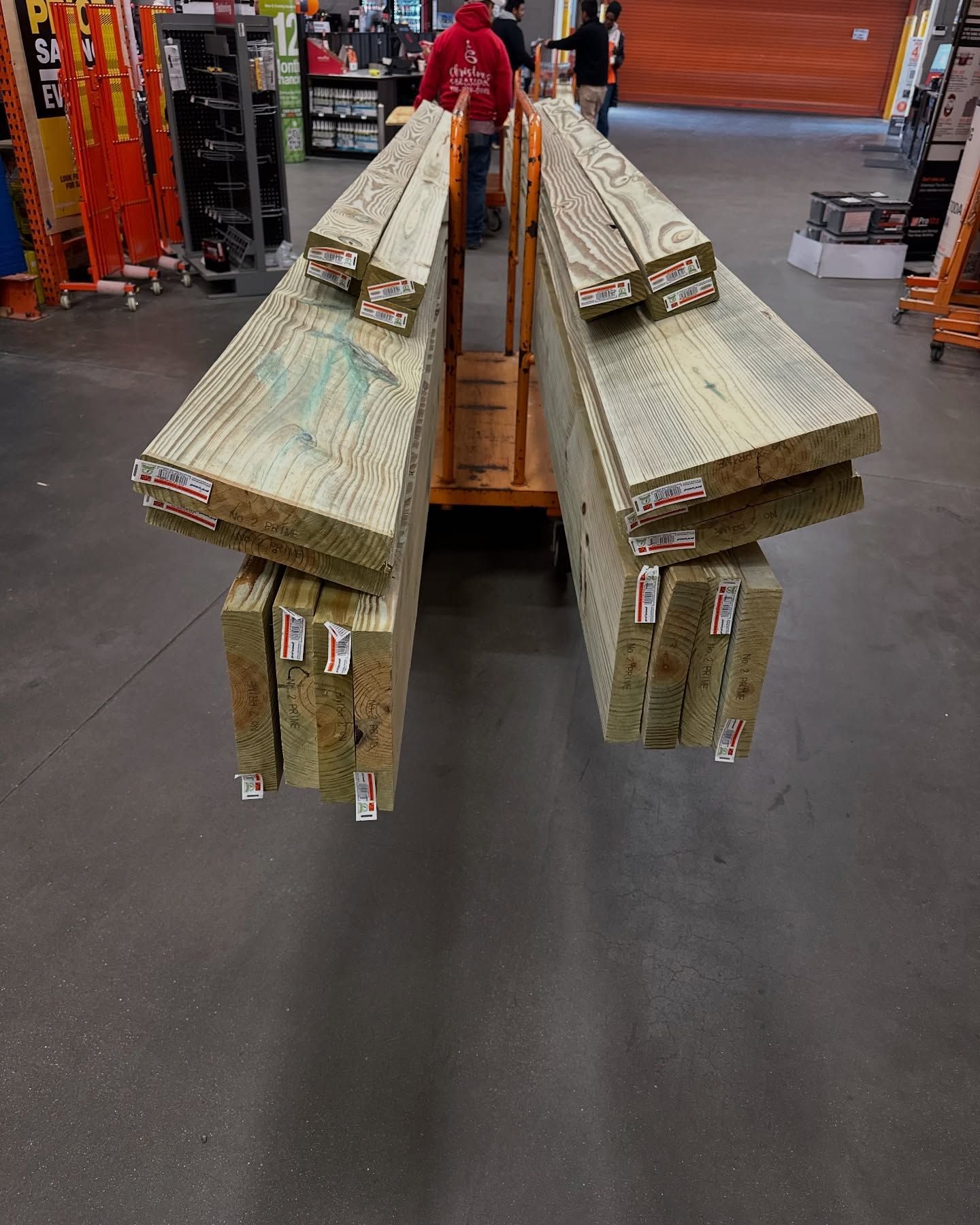 Lumber on a yellow cart inside a hardware store; wood planks with price tags stacked.