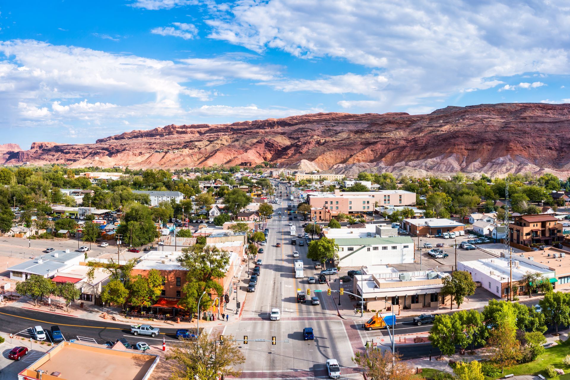 A sunlit aerial view of a sprawling residential neighborhood set against a backdrop of distant, rugged desert mountains.