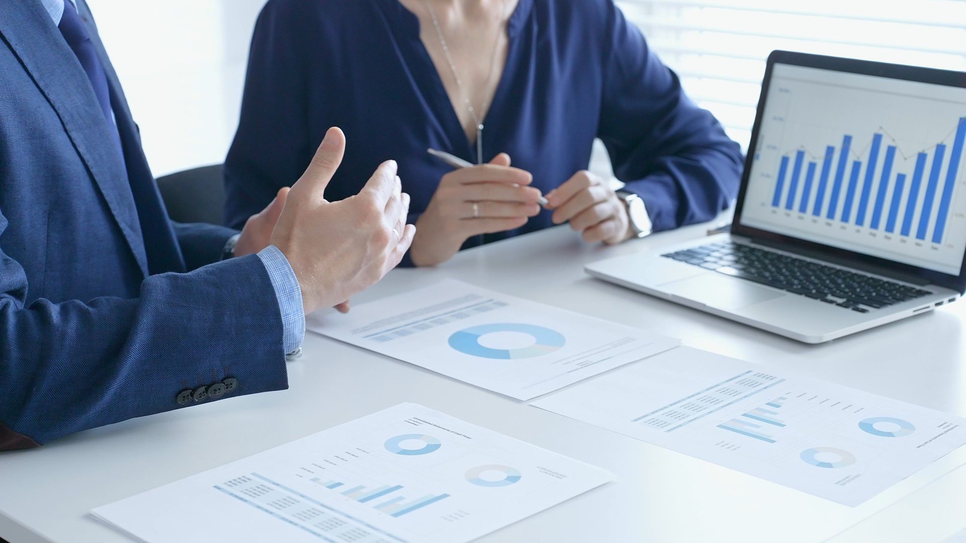 Business colleagues analyzing financial charts and bar graphs on paper documents and a laptop during a meeting.