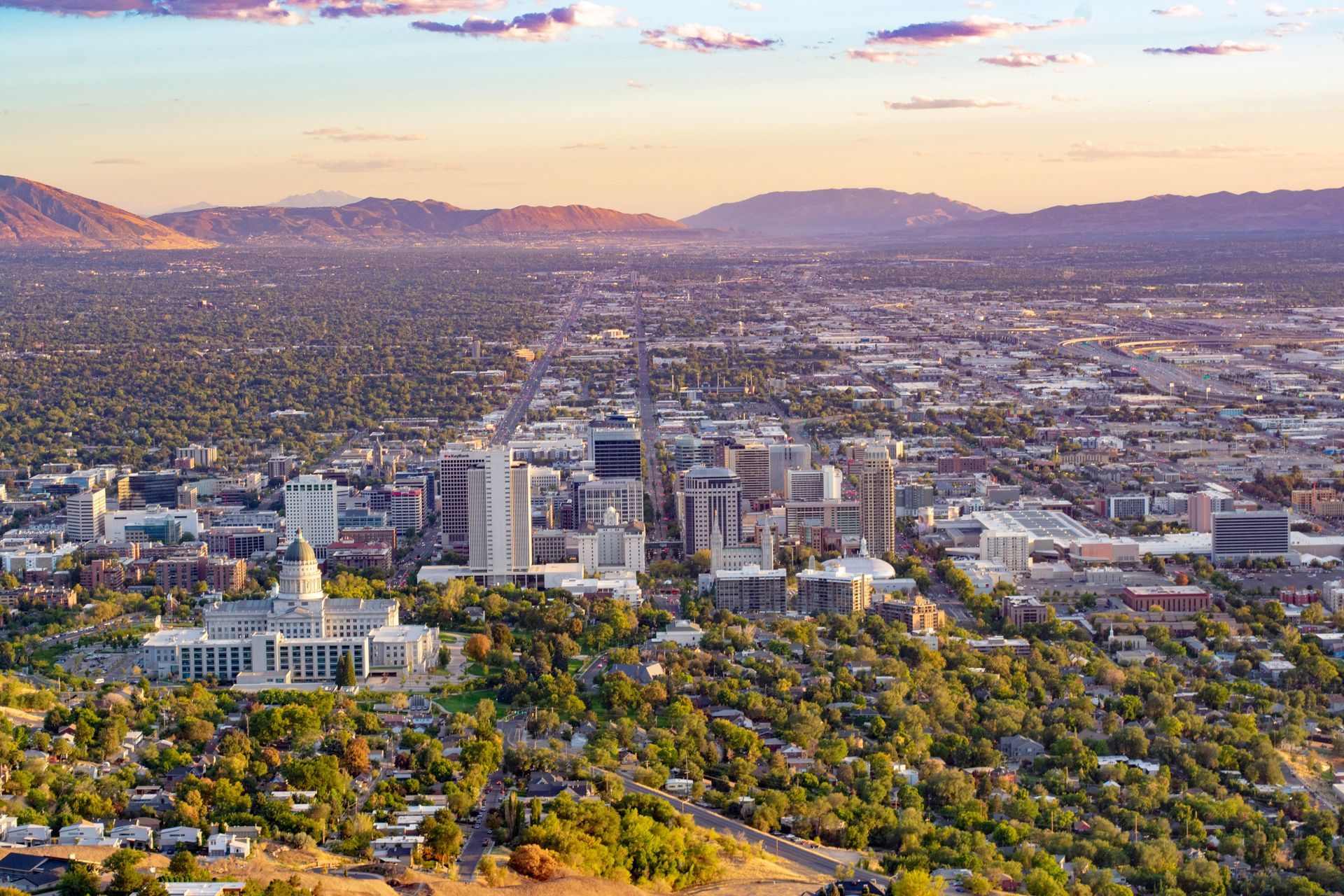 Aerial view of the Salt Lake City skyline with the Utah State Capitol building in the foreground under a golden sunset.