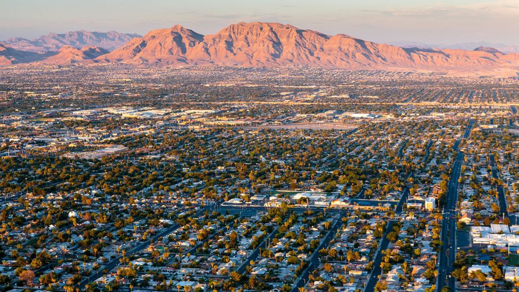 A sunlit aerial view of a sprawling residential neighborhood set against a backdrop of distant, rugged desert mountains. A sunlit aerial view of a sprawling residential neighborhood set against a backdrop of distant, rugged desert mountains.