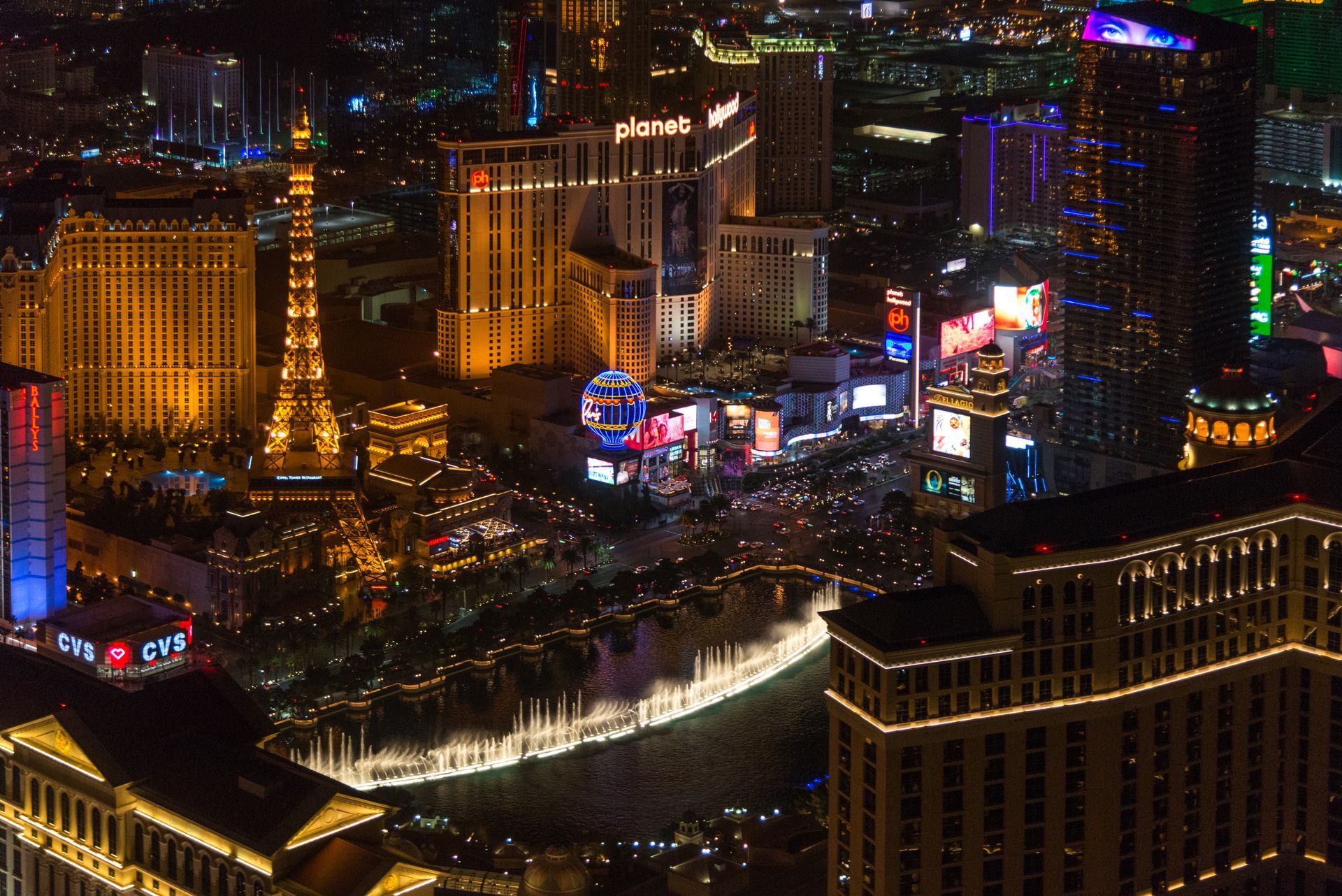 Two construction professionals in hard hats review a blueprint at a housing development site. Night aerial view of the Las Vegas Strip, featuring the illuminated Bellagio fountains and surrounding casino resorts.