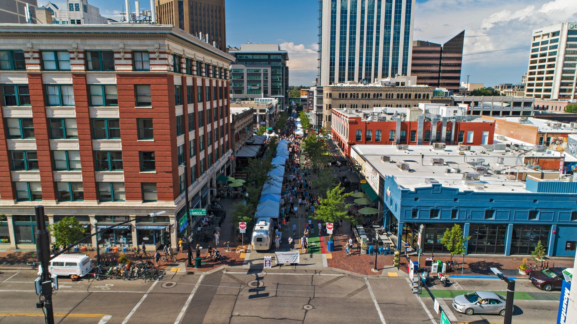 High-angle view of a bustling city street with shops, pedestrians, and cars on a sunny day.