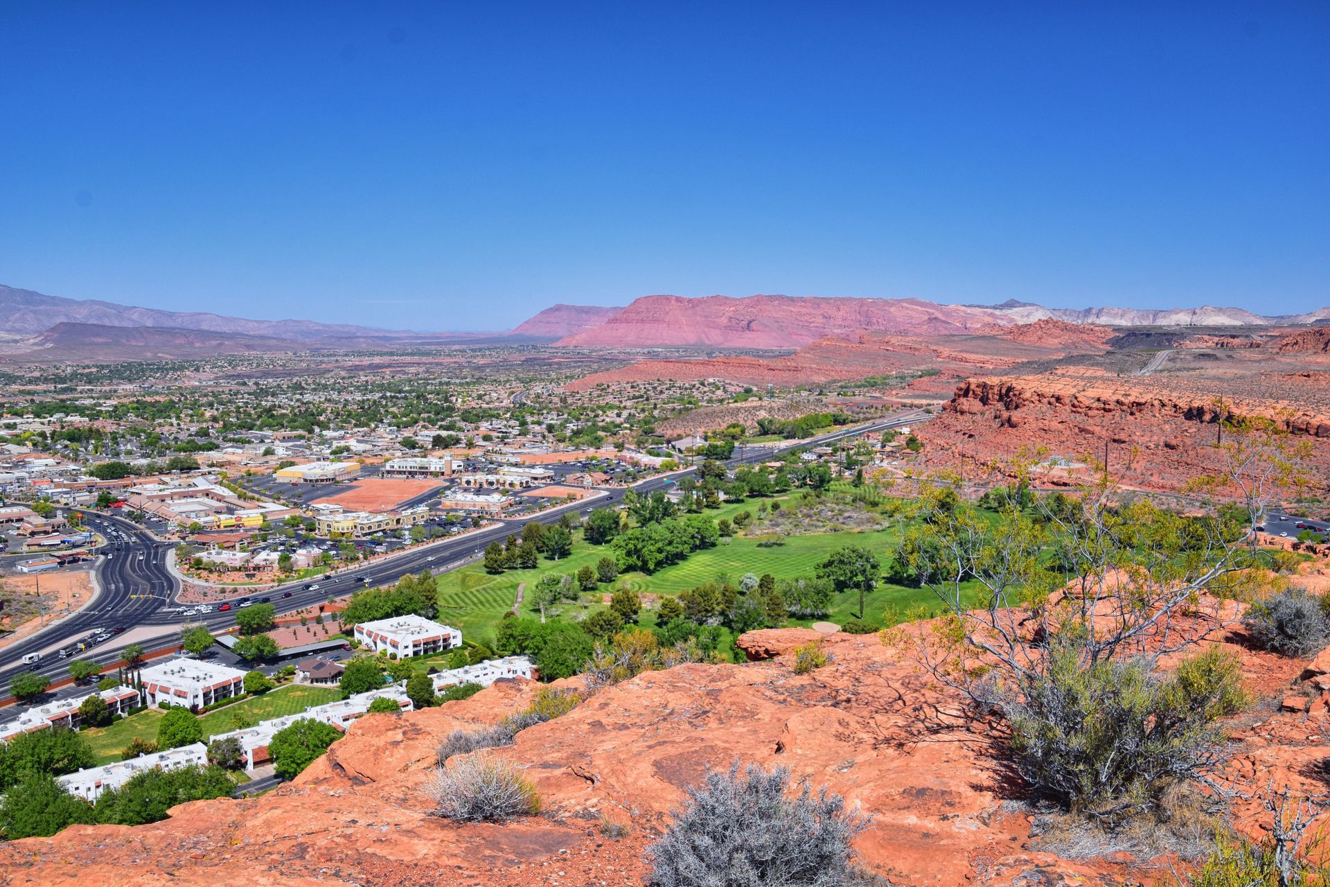 An aerial view of a sprawling urban area with dense housing, flat-roofed buildings, and dry mountains in the background.