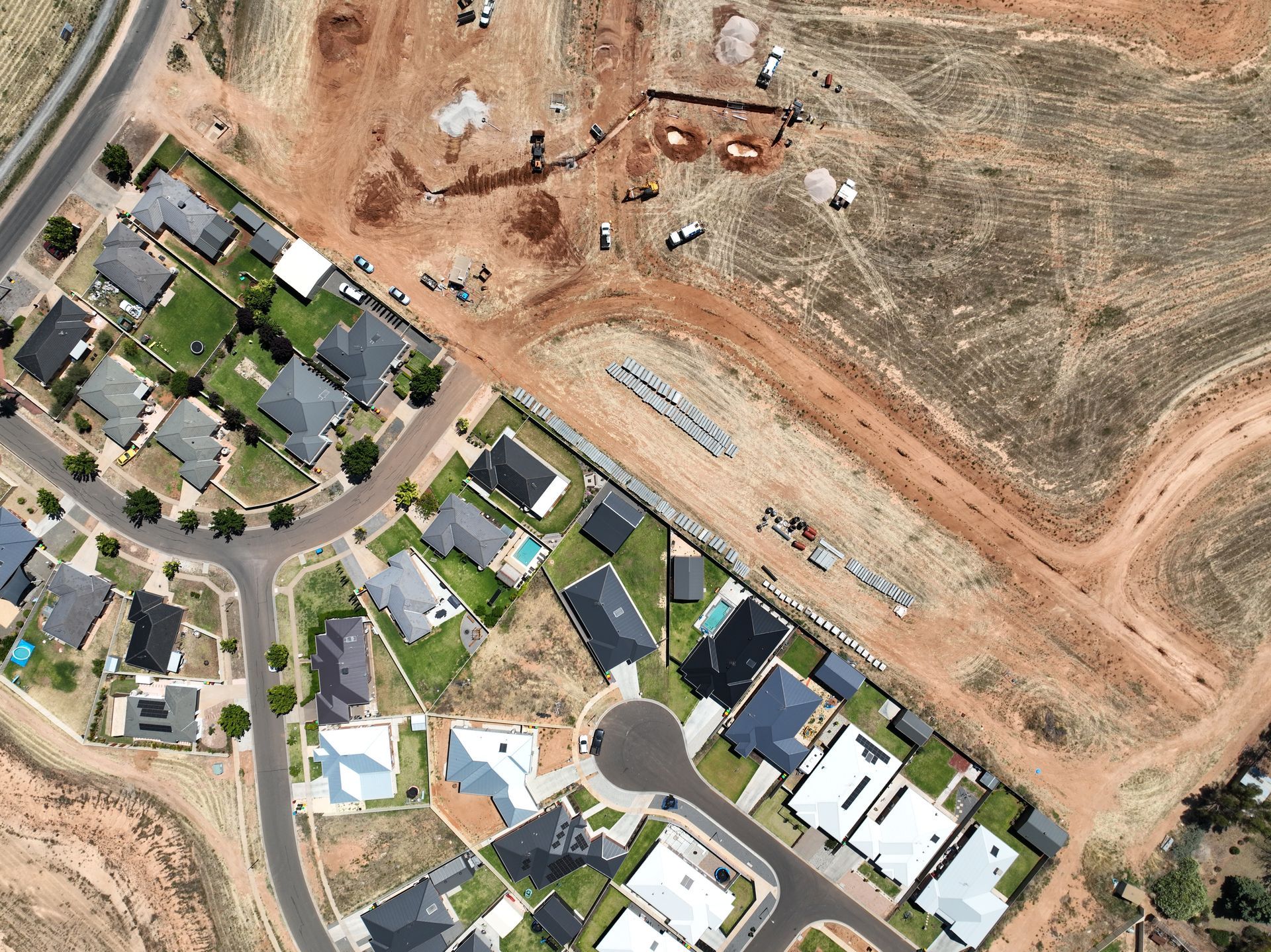 An aerial view shows a suburban neighborhood bordering a large, active construction site with dirt roads and equipment.