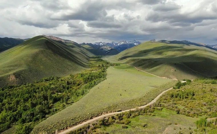 A gravel road winds through a lush, green mountain valley beneath a dramatic, cloudy sky. A gravel road winds through a lush, green mountain valley beneath a dramatic, cloudy sky.