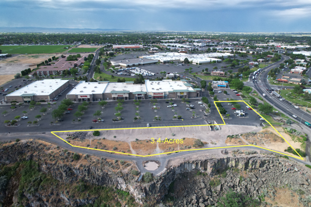 An aerial view of a vacant plot of land highlighted in yellow, situated next to a commercial shopping center and a cliff.