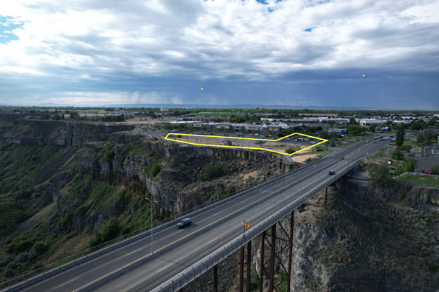 An aerial view of a canyon bridge next to a yellow-outlined vacant lot under a cloudy sky.