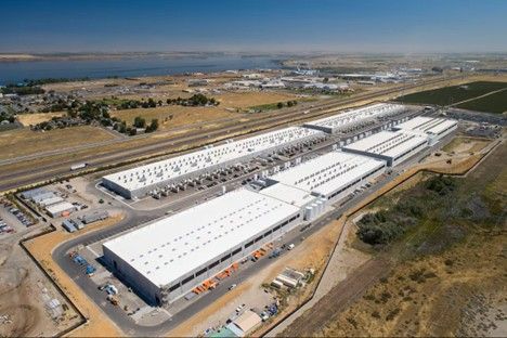 An aerial view of a massive, rectangular white-roofed industrial warehouse complex set in a dry, open landscape.
