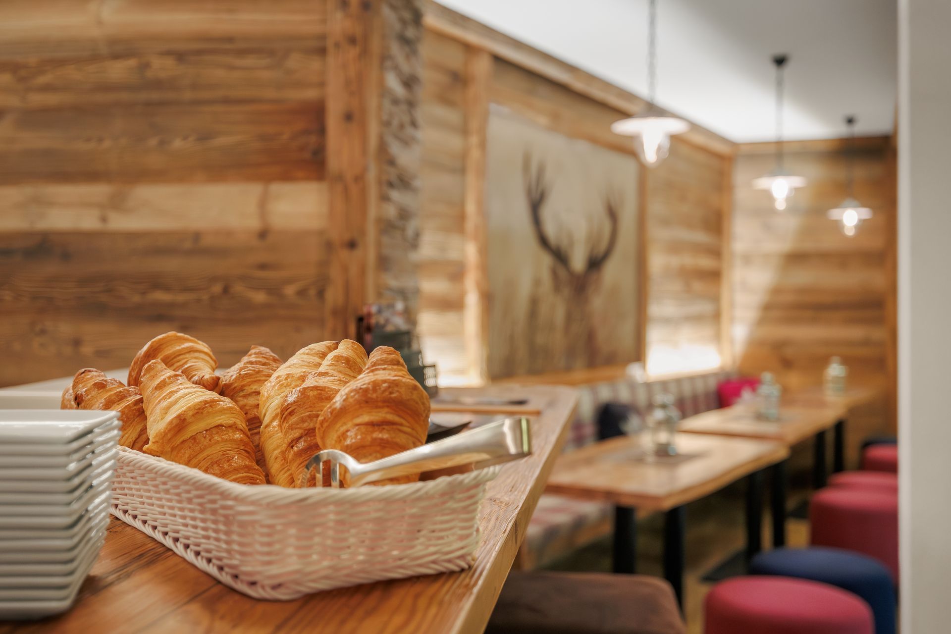 Basket of croissants on a wooden table in a cozy cafe with wood-paneled walls and hanging lights