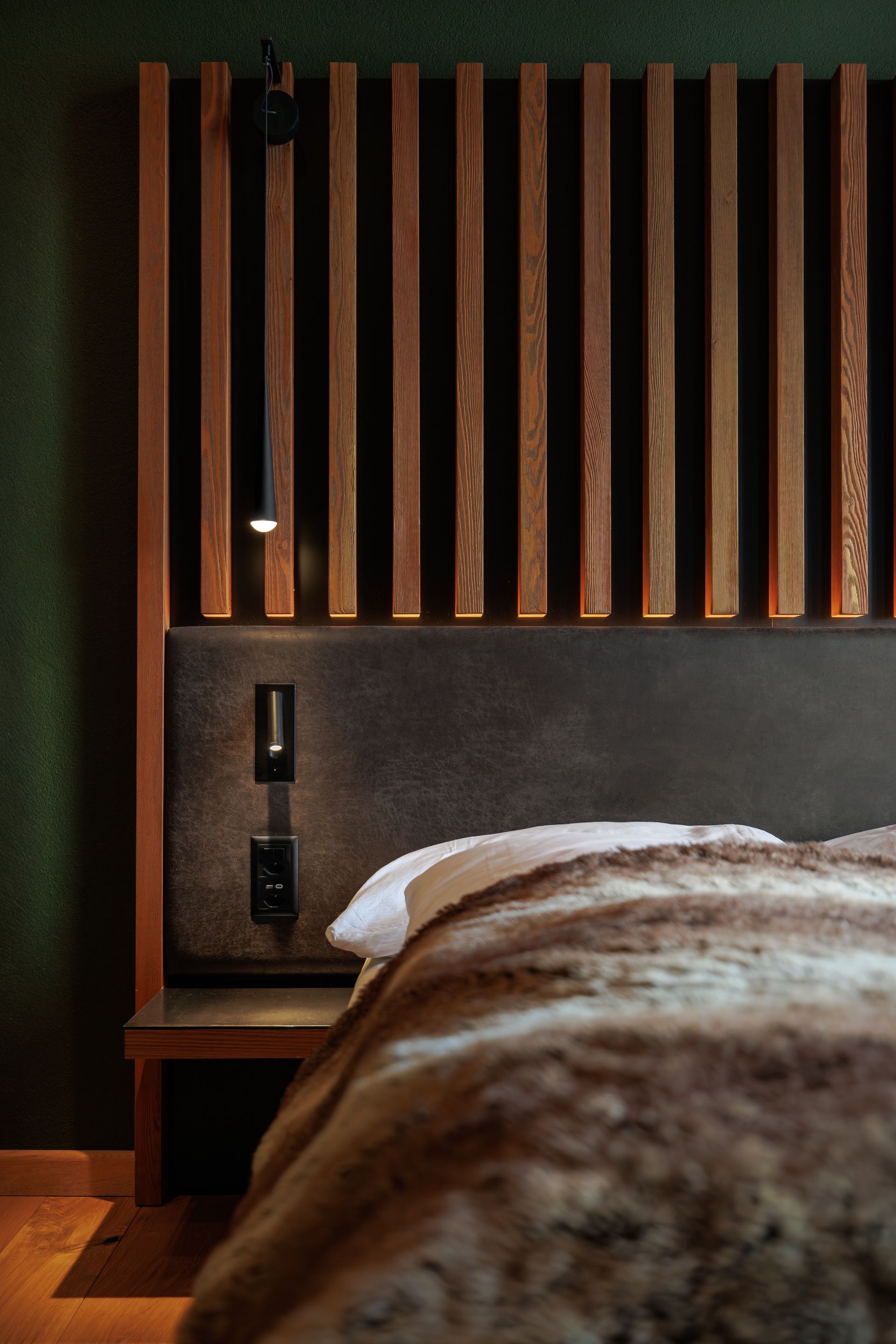 Modern bedroom with a wooden slat headboard, bedside light, and fur blanket on the bed