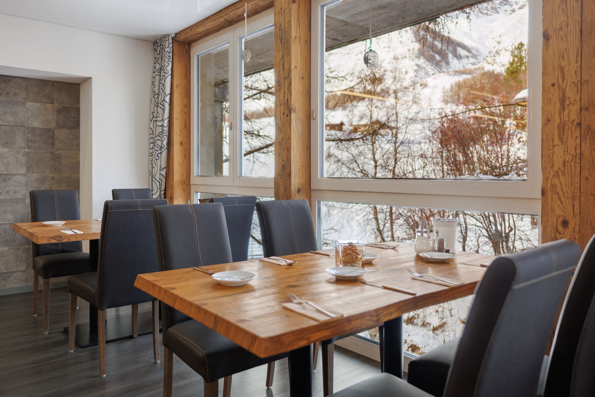 Modern dining area with wooden table, dark chairs, and large windows overlooking a snowy landscape