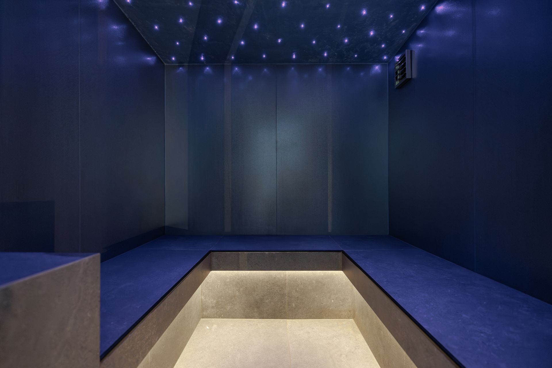 Dark blue room with star-like ceiling lights and a central sunken platform or pool area.