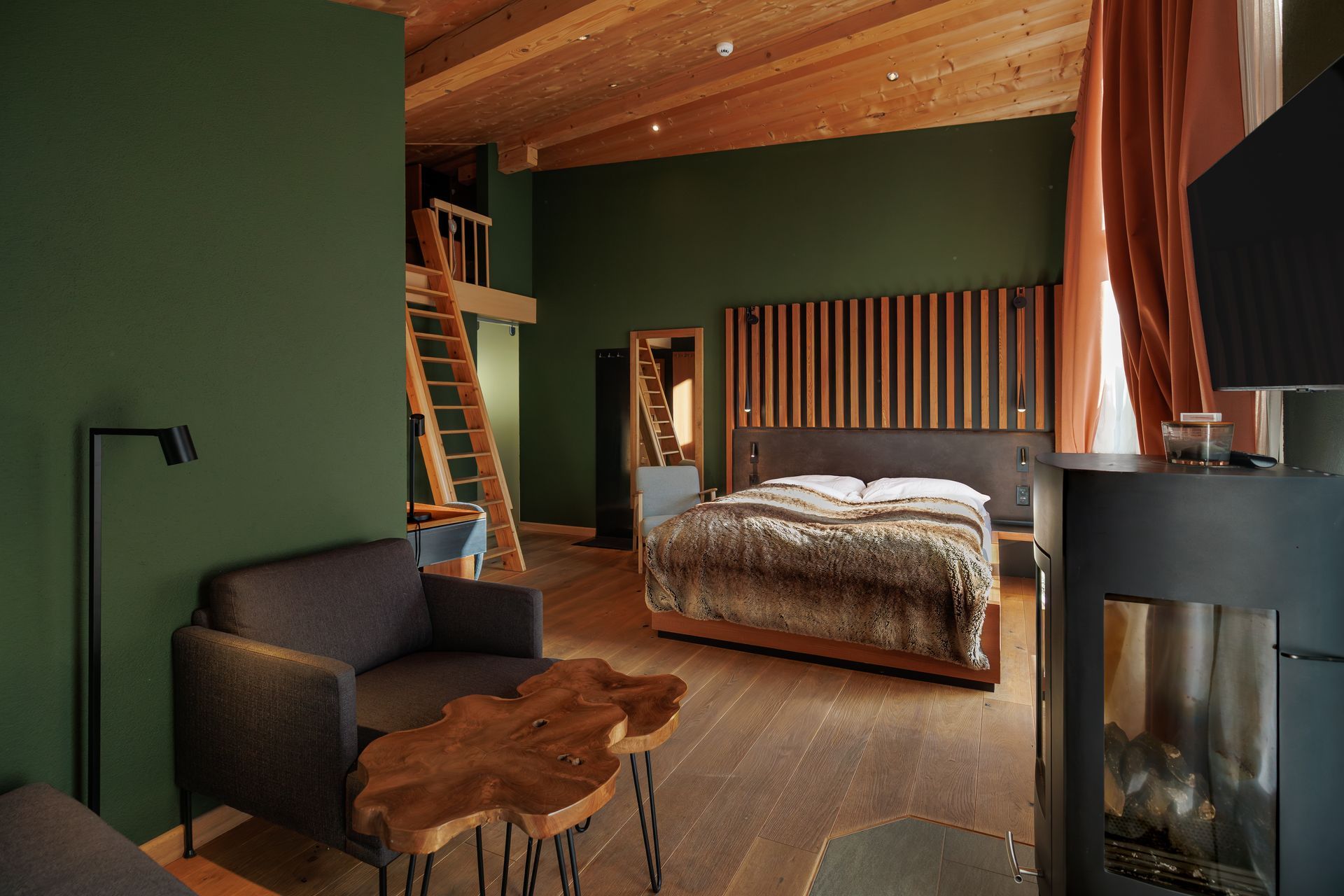 Cozy bedroom with wood-paneled ceiling, green walls, bed, sofa, staircase, and fireplace