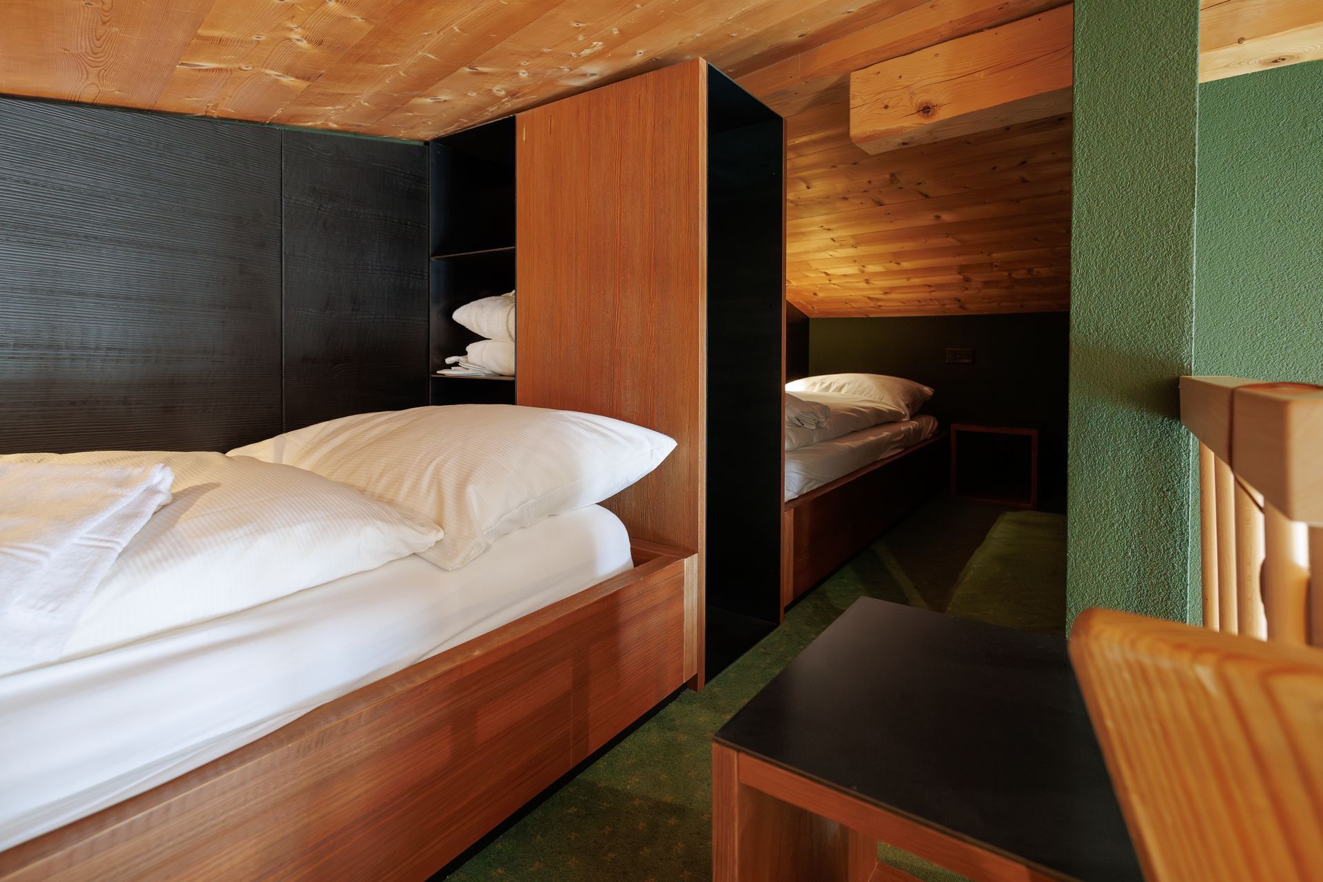 Compact wood-paneled bedroom with two beds, one in the foreground and one in the back.
